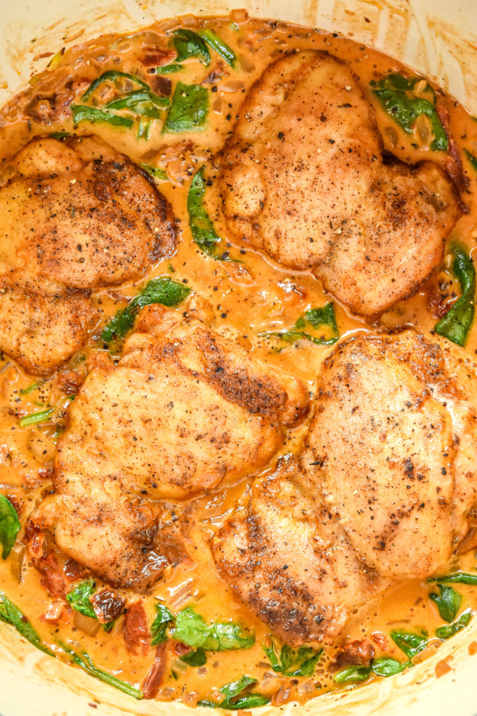 close up of cooked creamy tuscan chicken meal prep with sauce in a dutch oven.