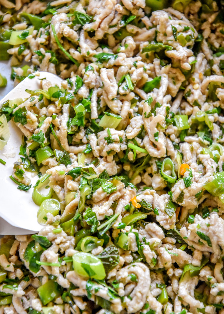close up of cooked chicken larb with fresh herbs.