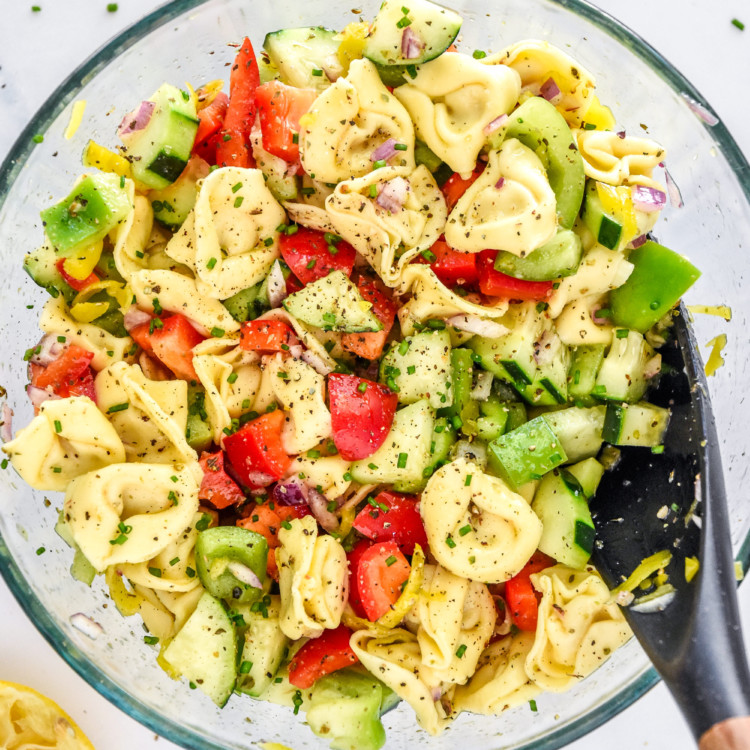 zesty italian tortellini pasta salad in a glass bowl with serving spoon.