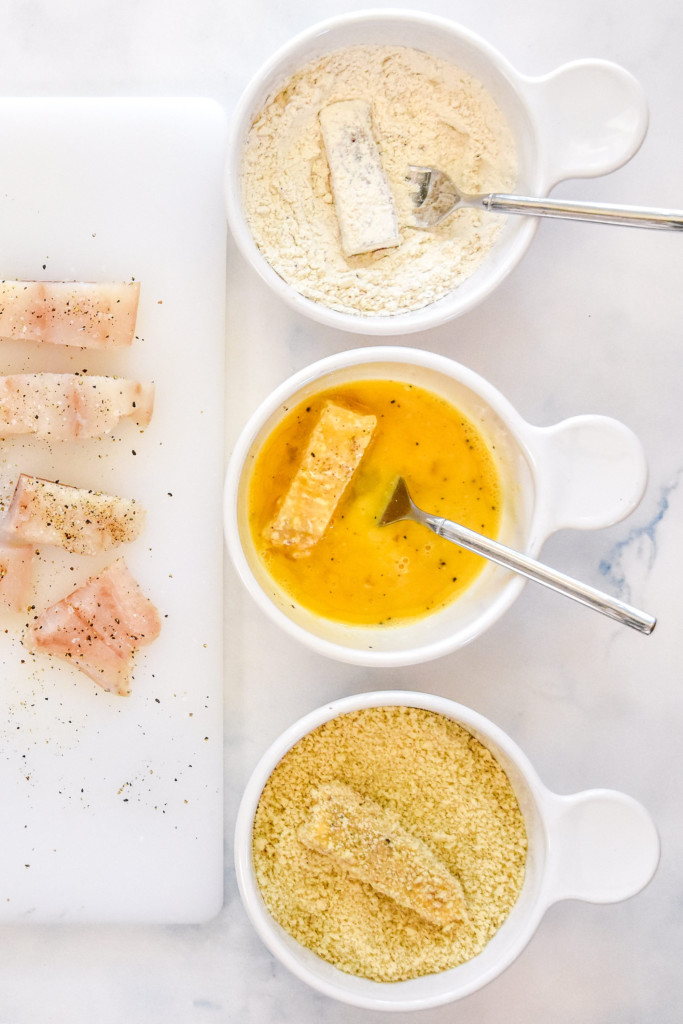 fish sticks being breaded one in each bowl of flour, egg and breadcrumbs.