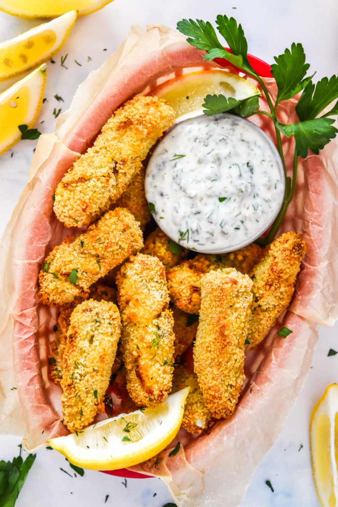 baked cod fish sticks with yogurt tartar sauce in a basket lined with food paper.
