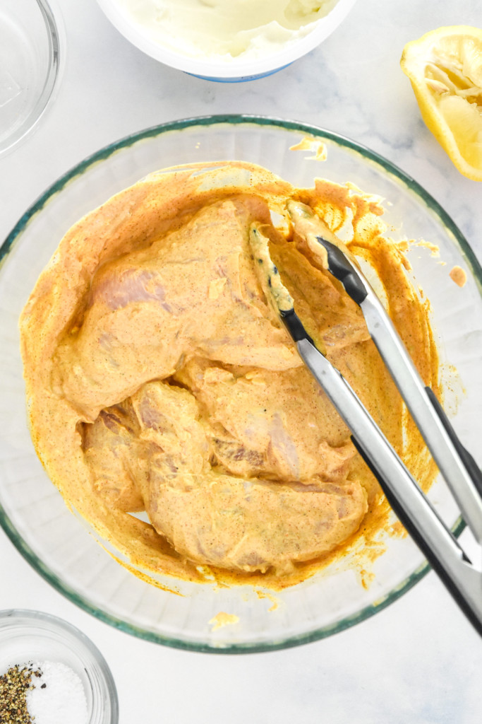chicken breasts in a yogurt marinade in a glass bowl.
