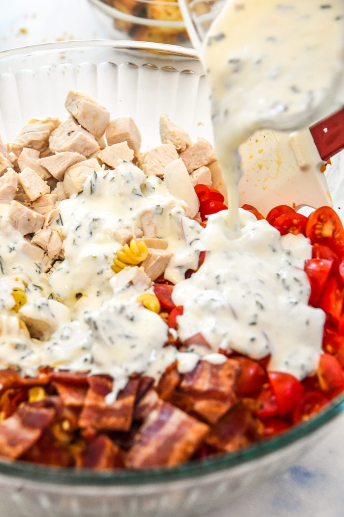 pouring dressing over the pasta salad.