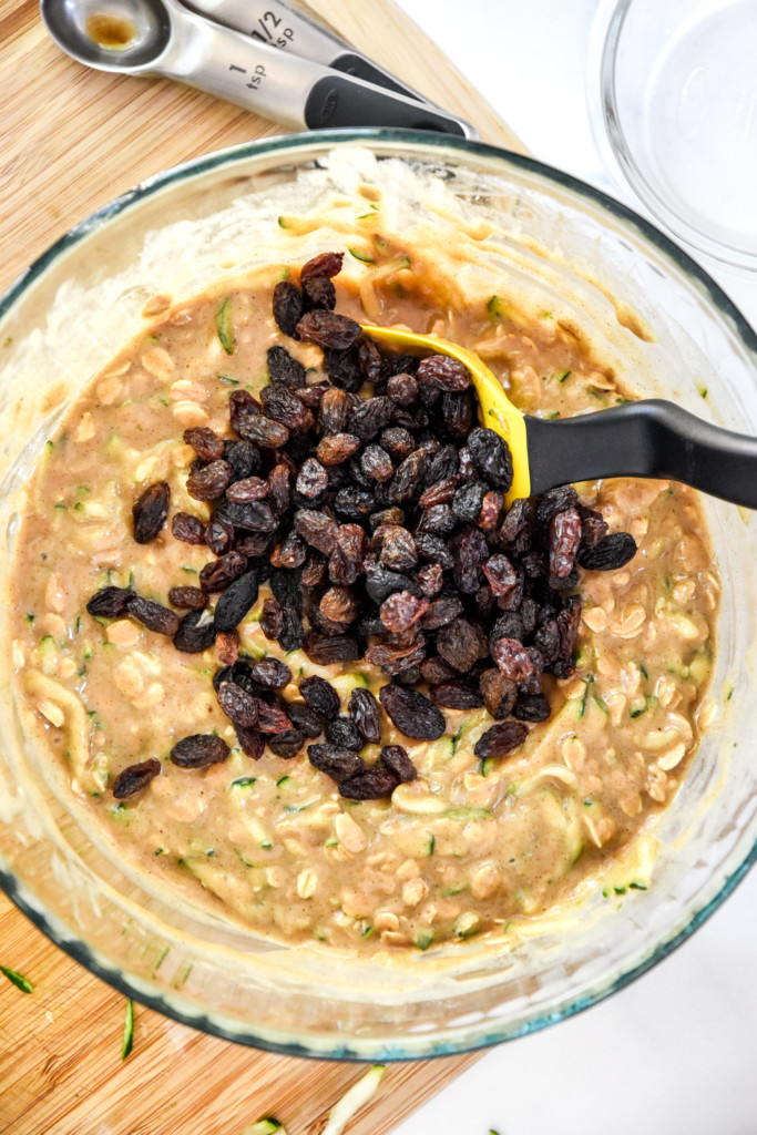 folding the raisins into the batter in a glass bowl for the cinnamon raisin zucchini coffee cake.
