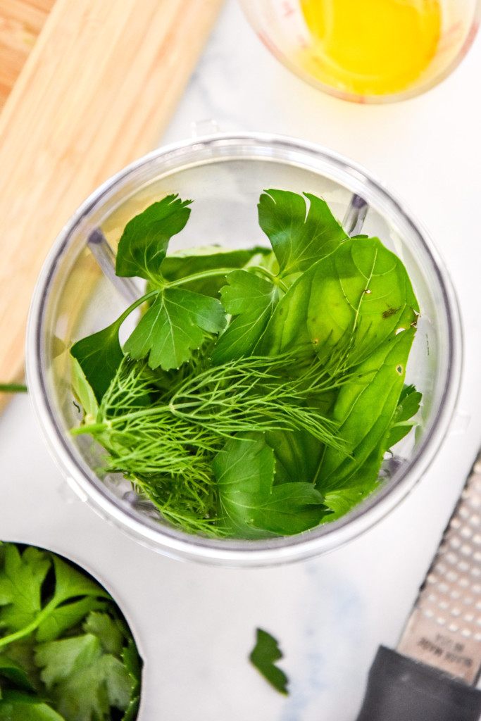 fresh green herbs in a nutribullet cup before blending.