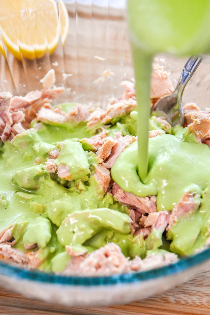 pouring the sauce into the tuna to make the green goddess tuna salad.