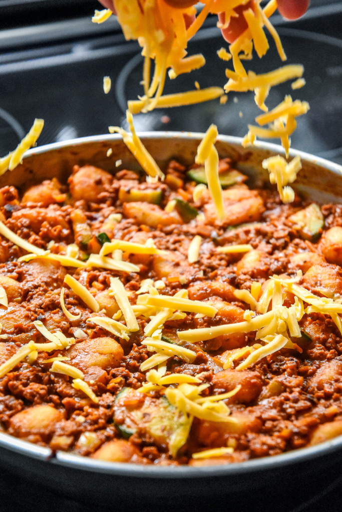sprinkling shredded cheese on the gnocchi and soy chorizo mixture.