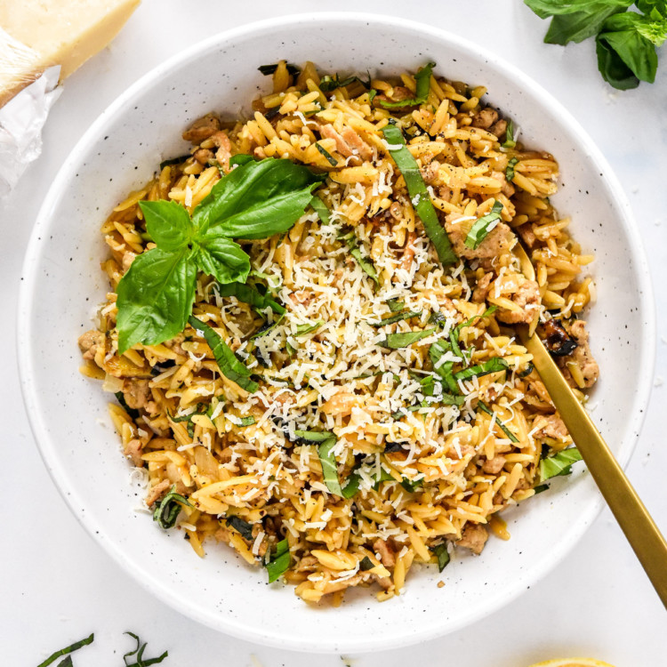Ground Turkey Zucchini Orzotto with fresh basil on top in a white bowl with fork.