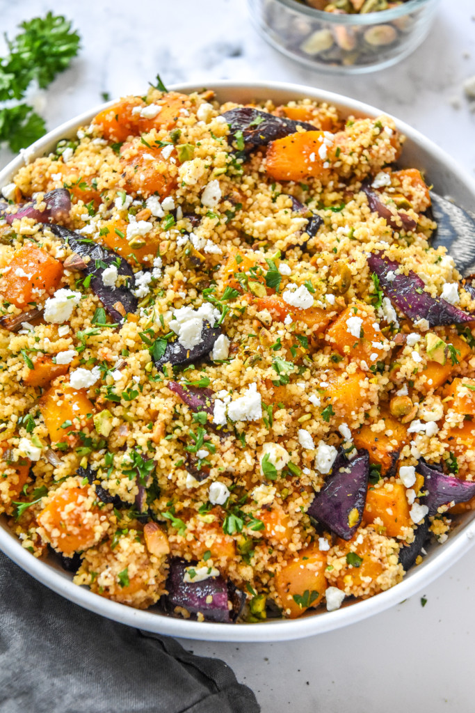 roasted butternut squash couscous salad in a glass bowl with a wooden spoon.