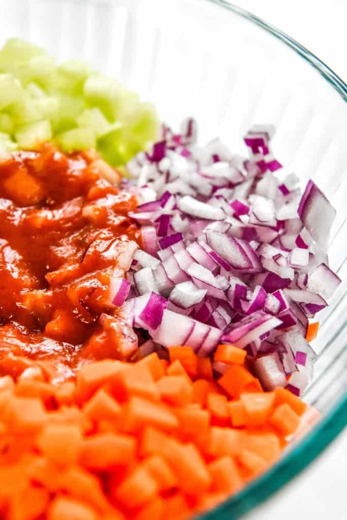 close up of red onion carrots and buffalo sauce in the bowl before mixing up.