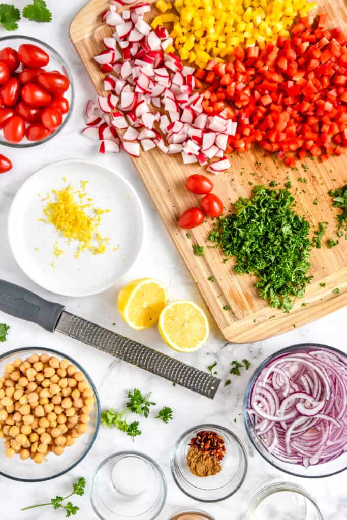 chopping vegetables and herbs on a wooden cutting board and zesting a lime for the make-ahead vegan chickpea salad.