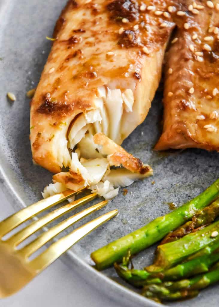 flaky Ginger Soy Tilapia and Broiled Asparagus on a plate with gold fork.