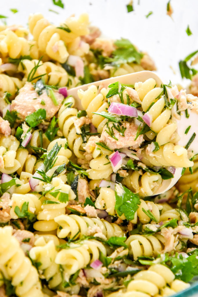 mixed up lemon vinaigrette tuna pasta salad close up in a glass bowl.