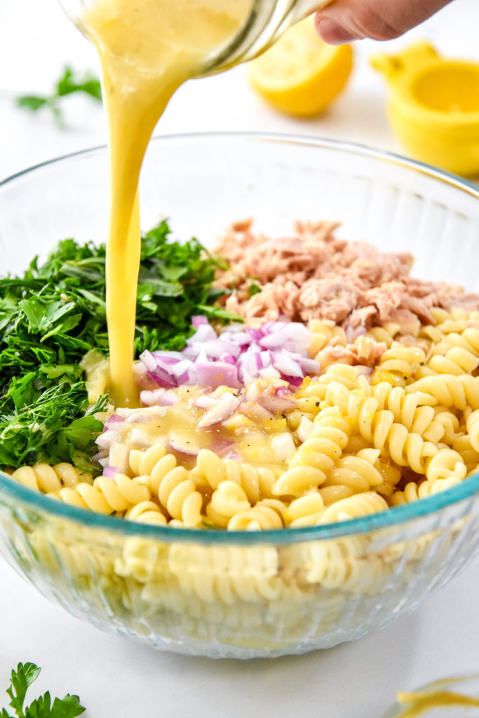 pouring dressing into the bowl of pasta, tuna, red onion and herbs.