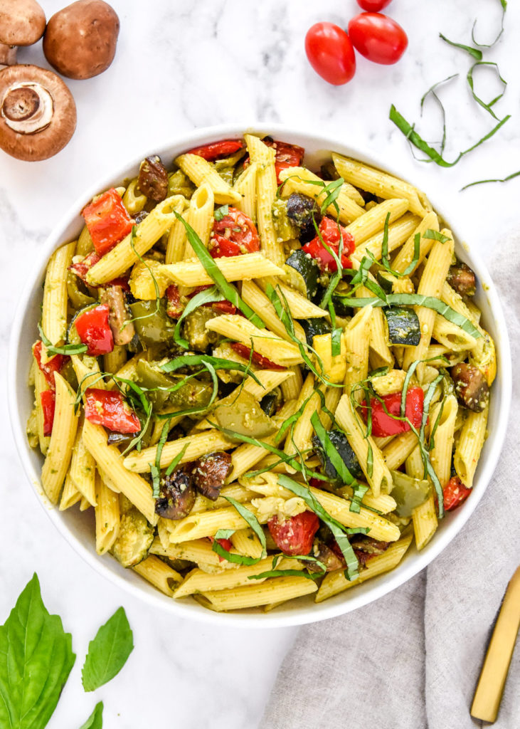 roasted veggie pesto pasta salad in a bowl with basil on top.