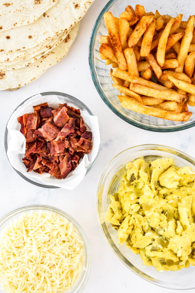 cooked ingredients like bacon and eggs in bowls before assembling breakfast burritos.