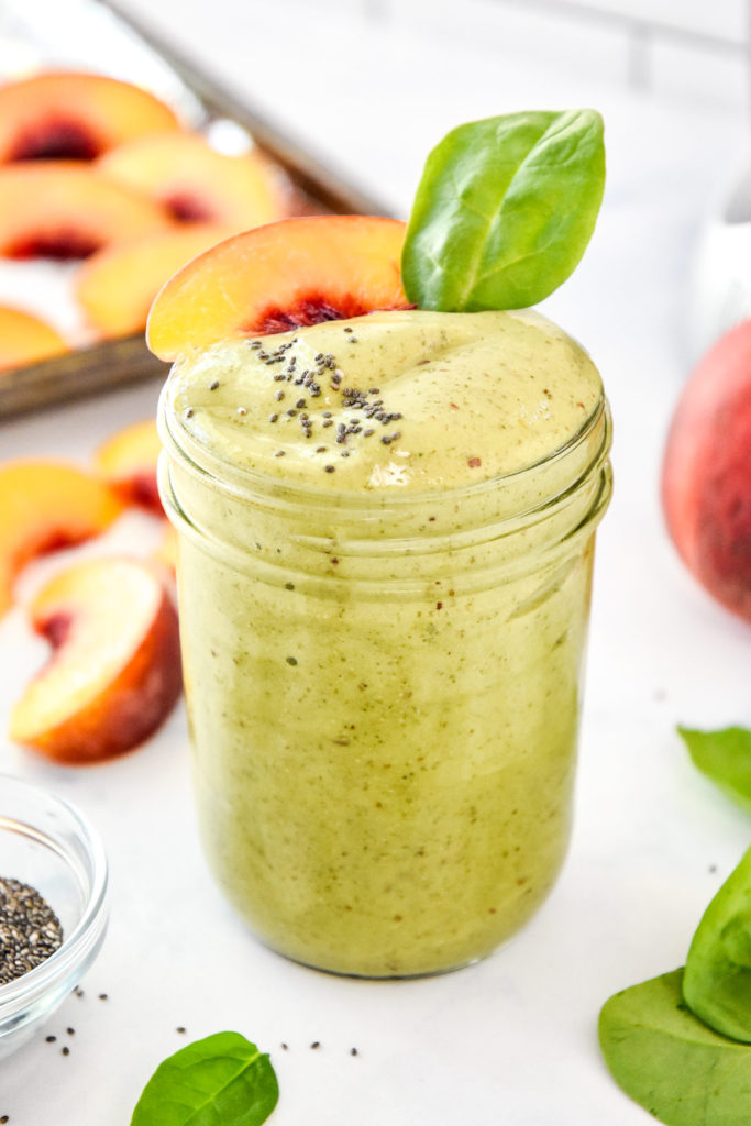 peaches and green protein smoothie with chia seeds and a peach slice on top.