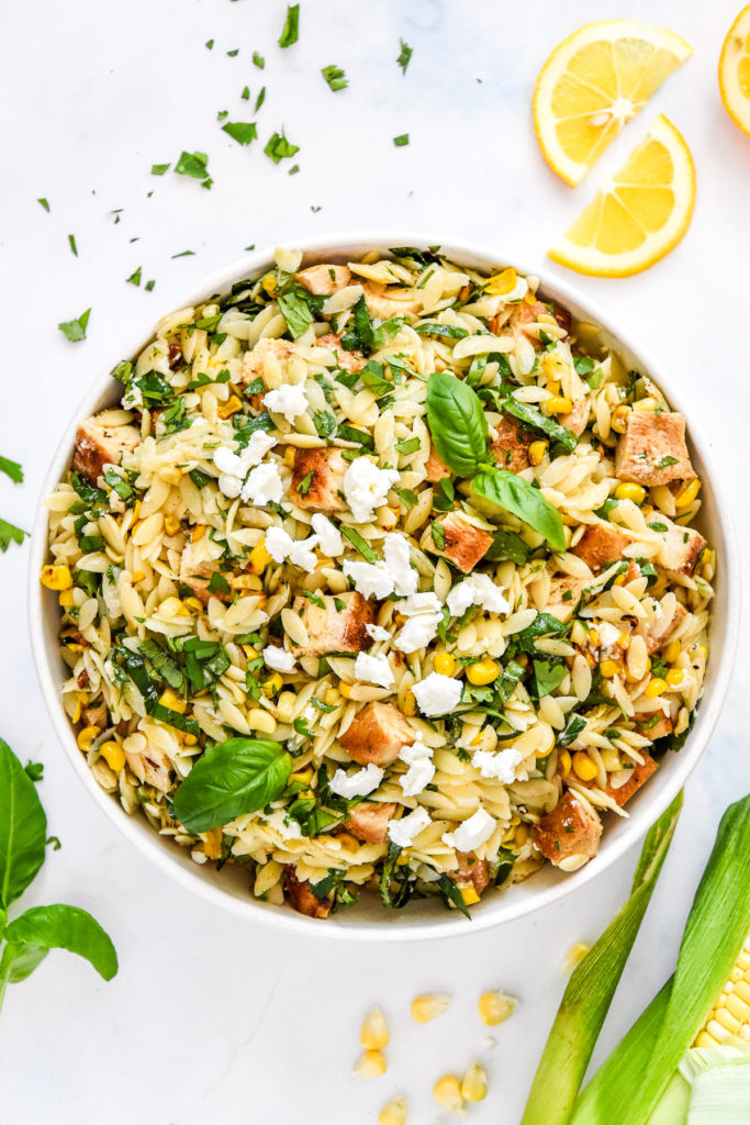 Lemony Chicken & Corn Orzo Salad in a large white bowl with fresh herbs on top.