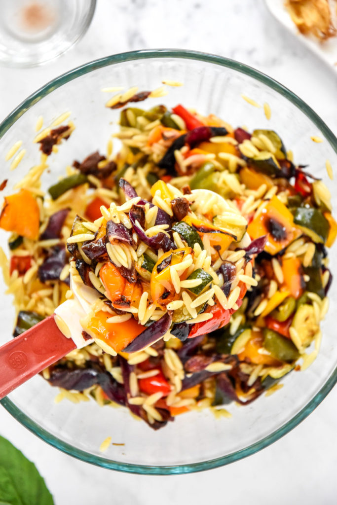 roasted vegetable orzo salad in a spoonful from a glass bowl. 
