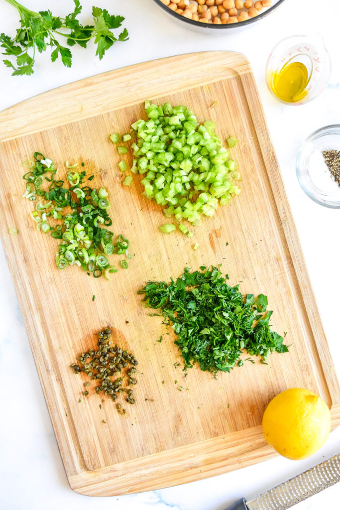chopped greens and capers on a bamboo cutting board.