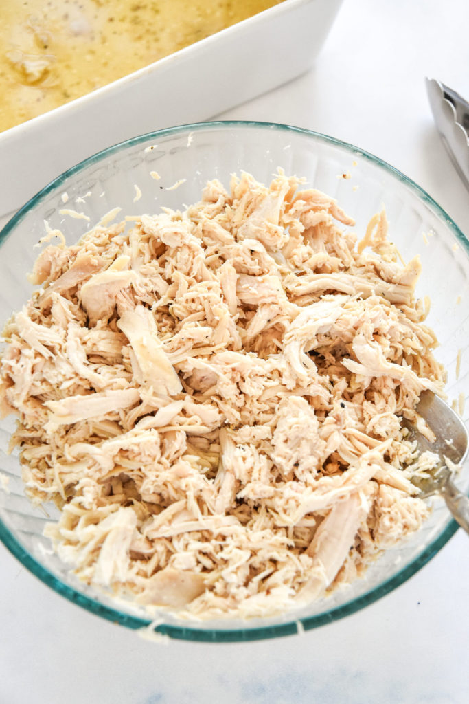 baked shredded chicken breast in a glass bowl with a large fork.