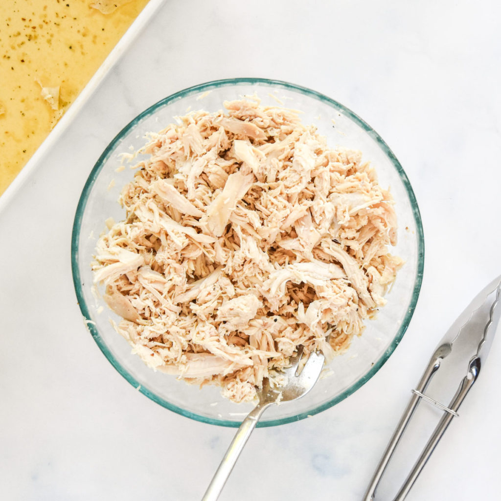 shredded chicken breasts in a glass bowl with large fork.