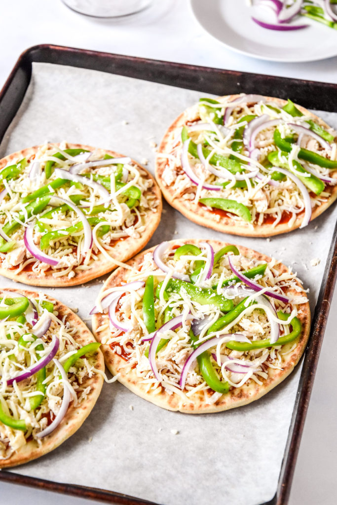 barbecue chicken flatbread pizzas with peppers and onions before baking.