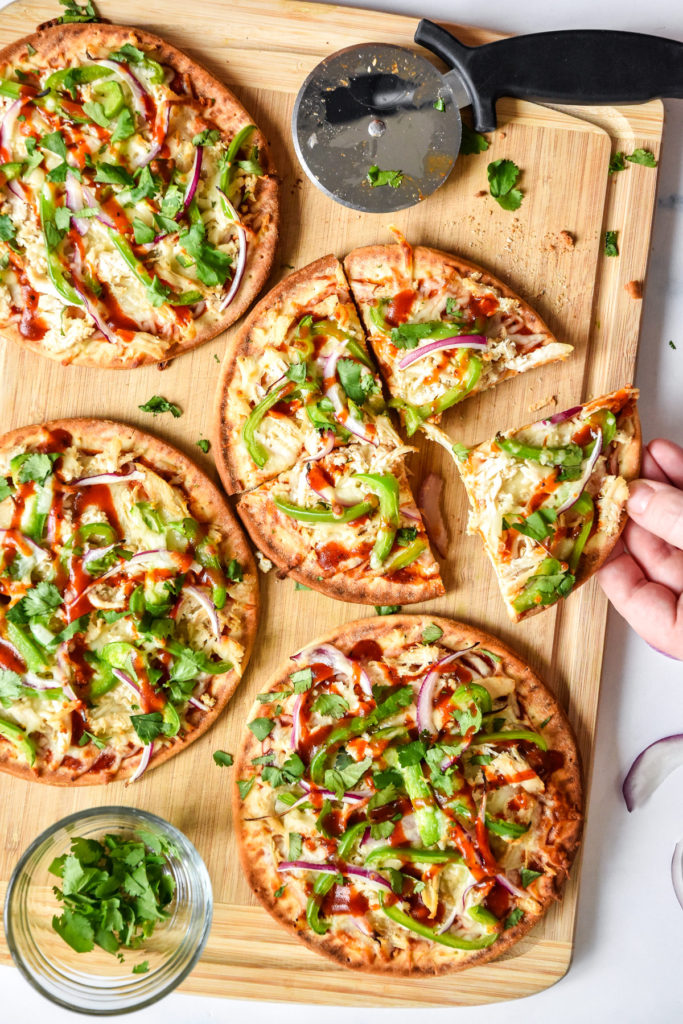 barbecue chicken flatbread pizzas on a cutting board one piece being removed.