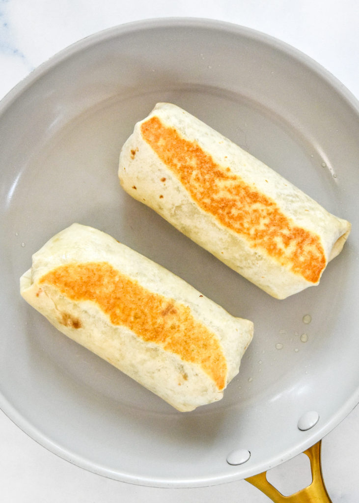 reheating the easy chicken bean burritos in a pan on the stovetop.