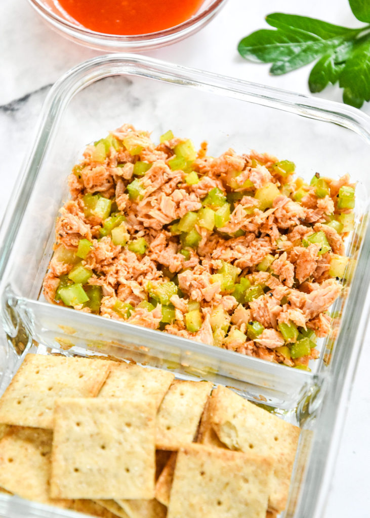 DIY flavored tuna packets made with buffalo flavor in a meal prep container with crackers.