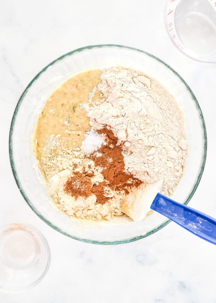 mixing up pancake batter in a large glass bowl with a rubber spatula.