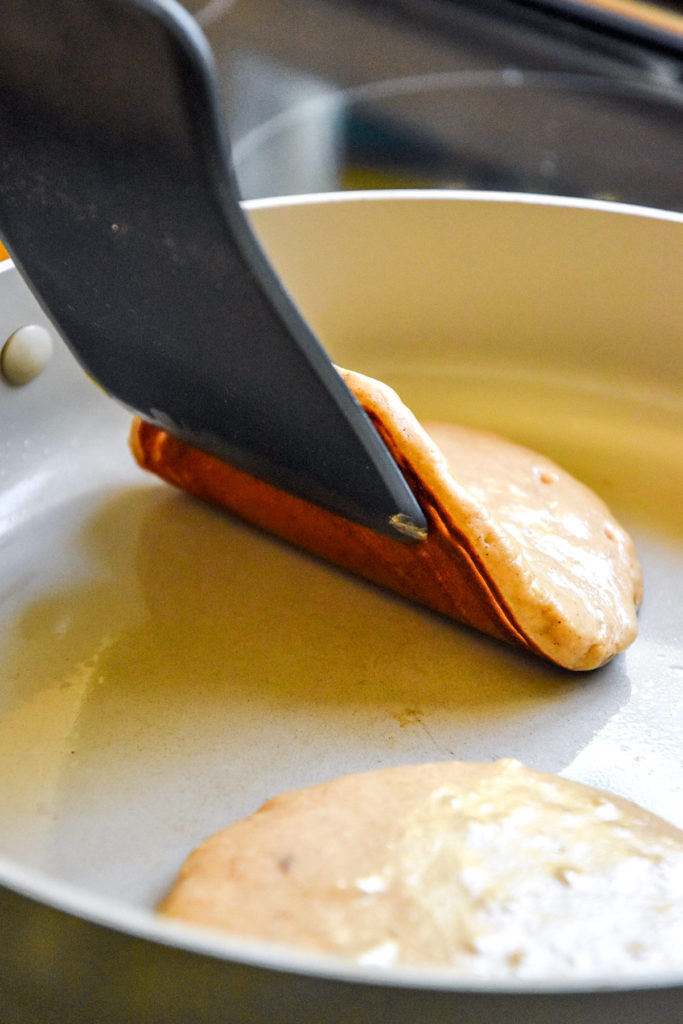 using a spatula to check how brown the pancakes are in the pan.