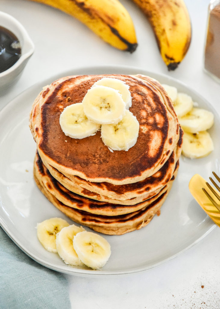 banana protein pancakes on a plate with sliced bananas on top.