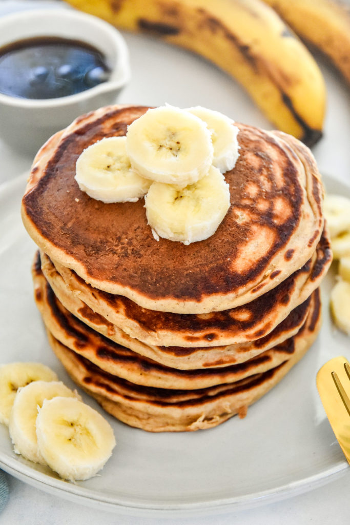 banana protein pancakes stacked on a plate with sliced bananas on top.