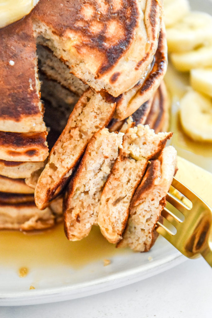 bite of sliced banana pancakes on a gold fork.