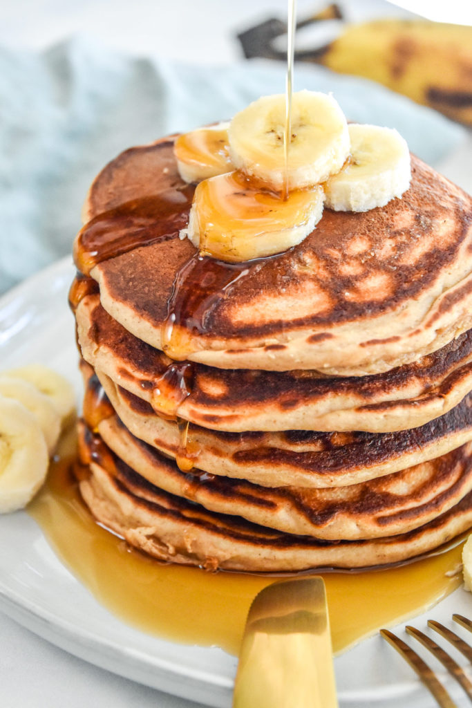 banana protein pancakes stacked on a plate with sliced bananas on top.