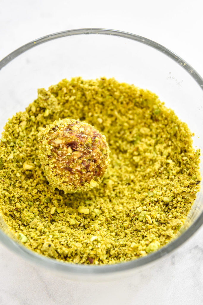 rolling a date ball in pistachio crumbs.