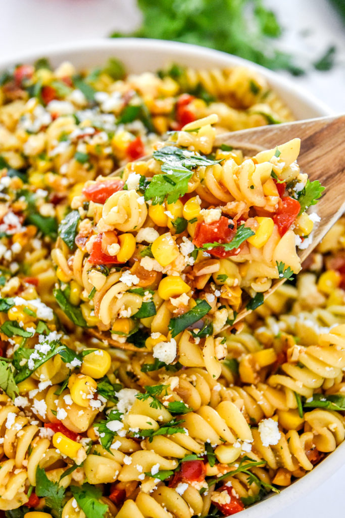 a scoop of pan roasted corn pasta salad in a wooden spoon.