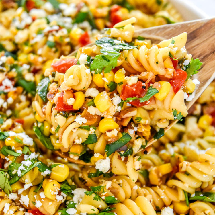 a scoop of pan roasted corn pasta salad in a wooden spoon.