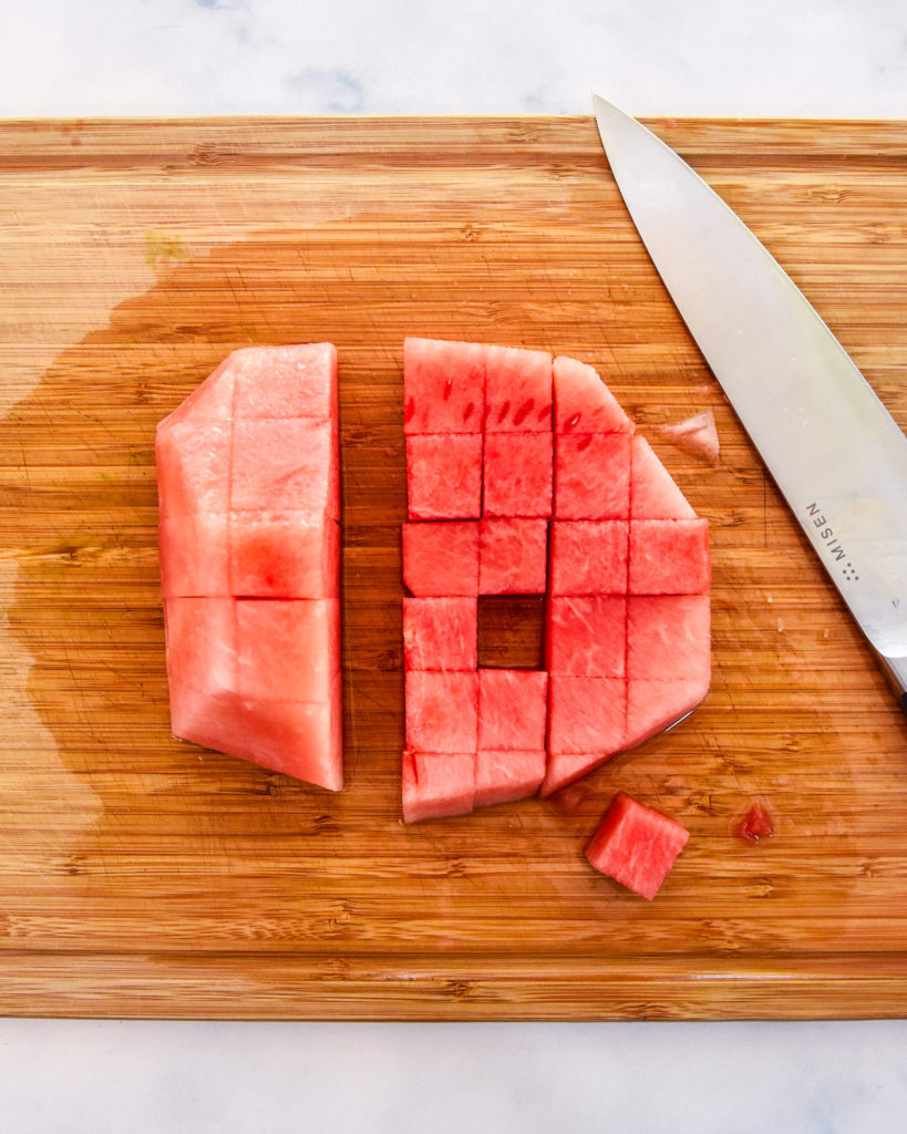 cutting watermelon into cubes on a cutting board.