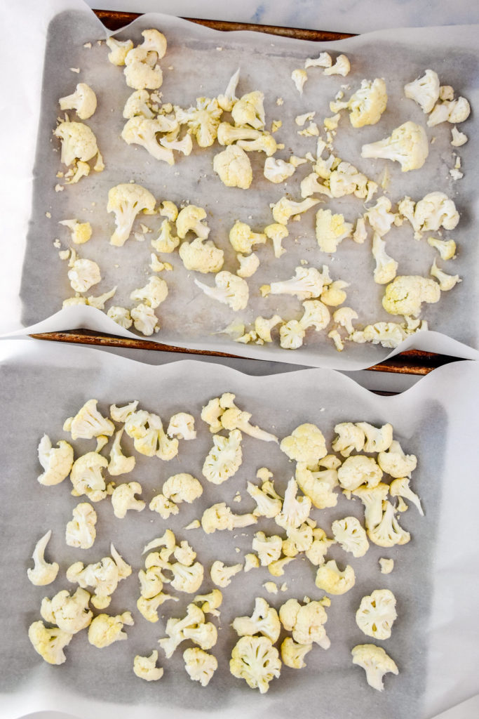 cauliflower florets spread over two sheet pans before baking.