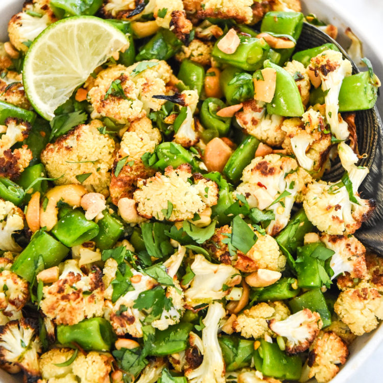 chili lime roasted cauliflower salad in a bowl with cilantro, cashews and a slice of lime on top.