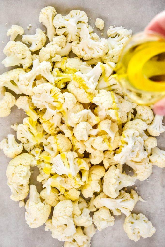 pouring olive oil on cauliflower florets.